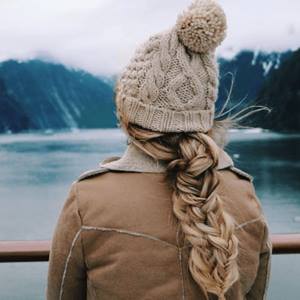 Blonde woman in winter coat and beige beanie stands at the edge of a lake in winter. 